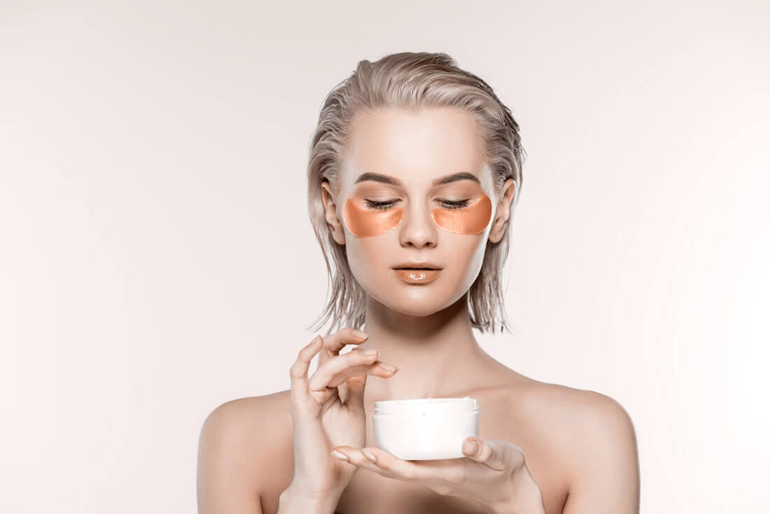woman-with-eye-patches-and-face-cream-in-plastic-c-UNMDWT2
